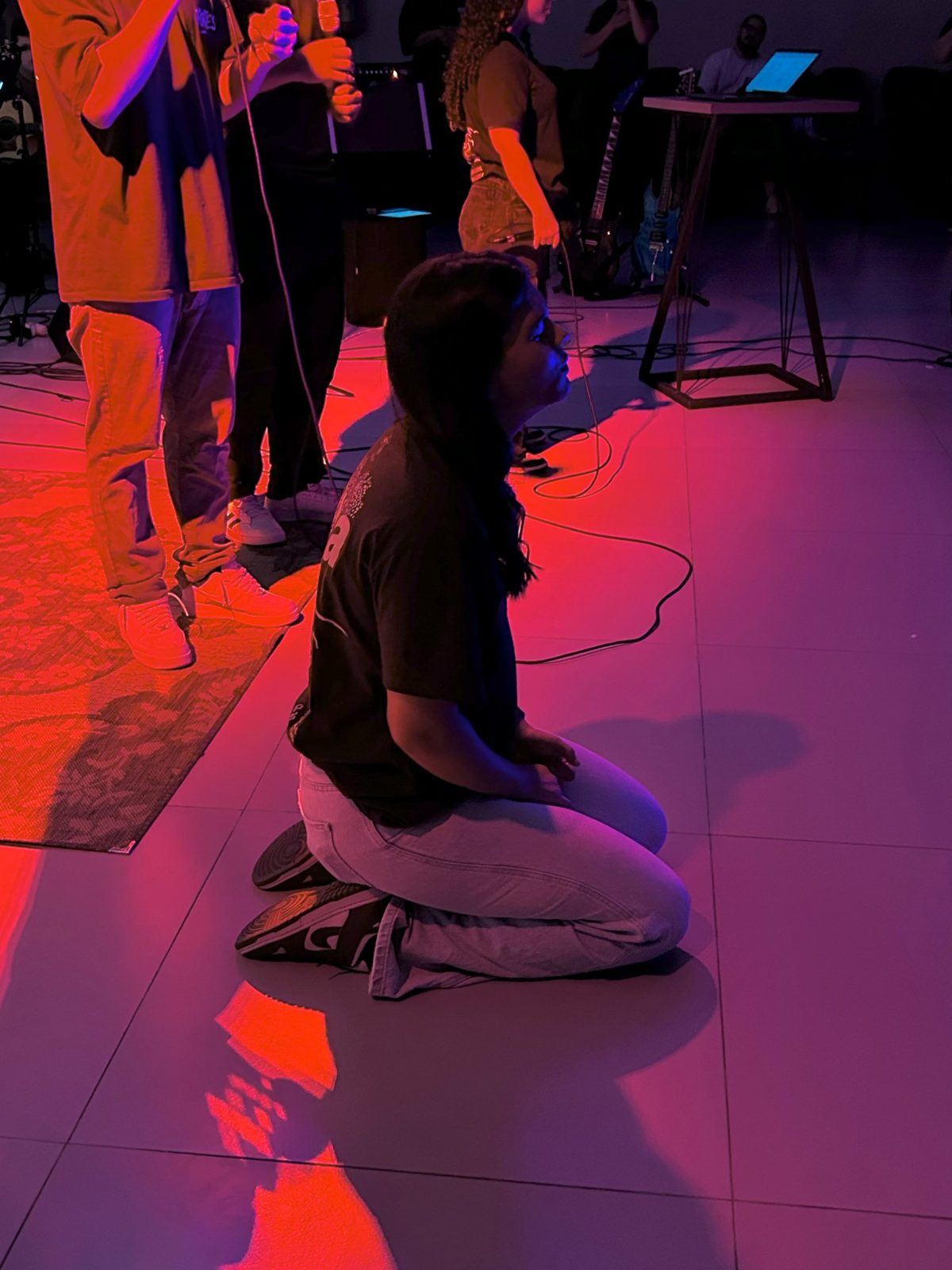 Jovem de joelhos em adoração sob luzes coloridas